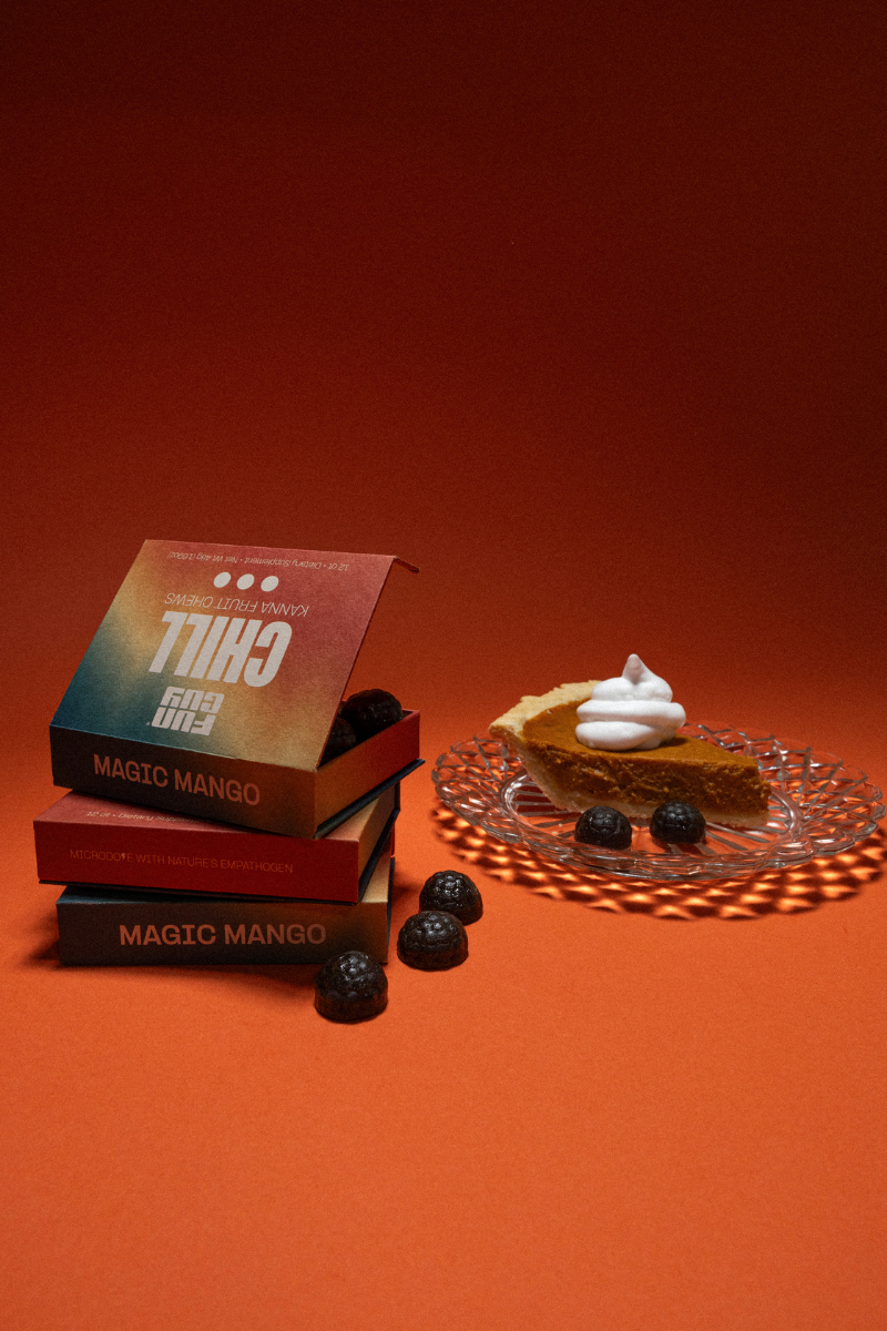 Three boxes of Fun Guy Chill Fruit Chews stacked on an orange surface beside chocolate candies and a slice of pie with whipped cream, all set against an orange background—the perfect treat for stress relief.