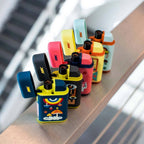 A row of vibrant Ignition Pocket Lighters - Nature Series by MK Lighter Company with playful, cartoon-like designs sits on a ledge, the blurred background highlighting the colorful refillable butane lighters in the foreground.