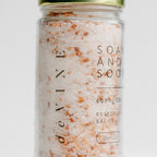 A clear jar of DeVINE Wellness Soak & Soothe Bath Salts holds pink and white bath soak with 600mg CBD, lavender essential oil, and epsom salt. It features a green metallic lid and is displayed against a plain background.