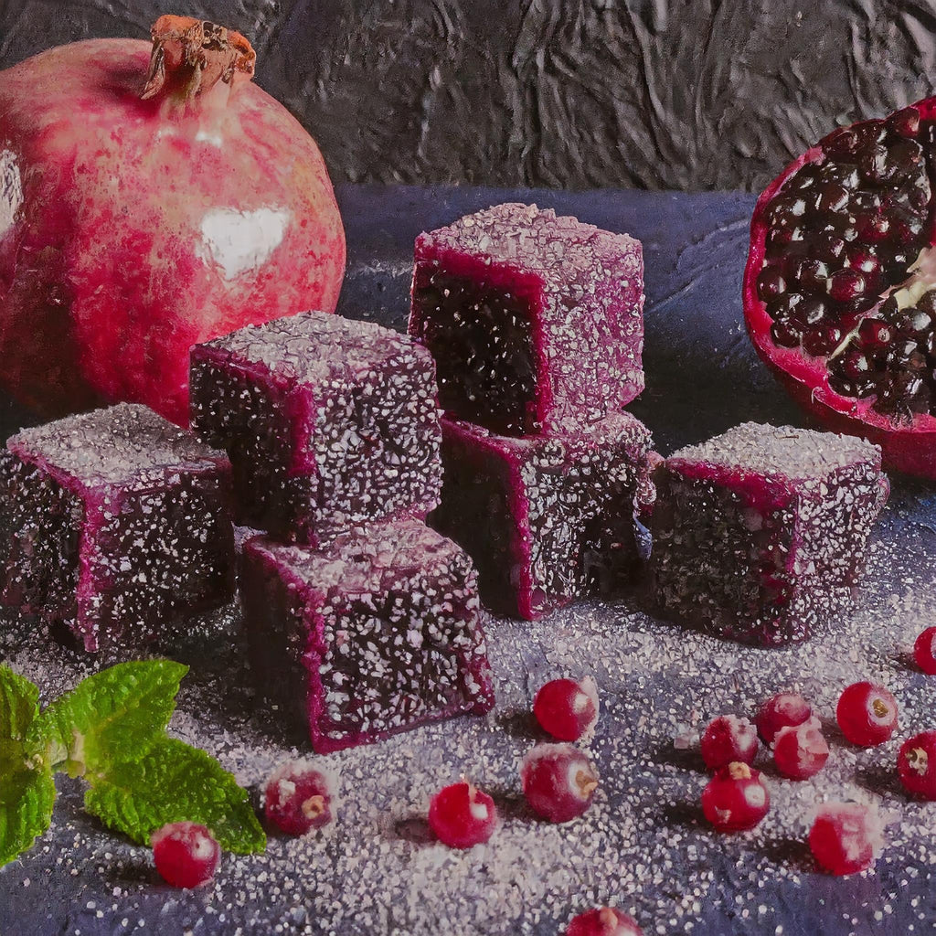 Sugared purple fruit jellies are arranged with whole and halved pomegranates, red berries, and mint leaves—an ideal way to showcase DeVINE Wellness GummieZzz as a delicious, natural CBD sleep aid against a dark textured background.