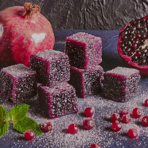 Sugared purple fruit jellies are arranged with whole and halved pomegranates, red berries, and mint leaves—an ideal way to showcase DeVINE Wellness GummieZzz as a delicious, natural CBD sleep aid against a dark textured background.