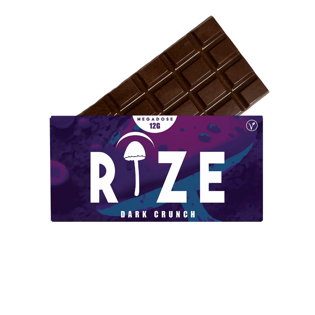 A Rize 12G Mushroom Chocolate Bar is partially unwrapped from a purple and blue wrapper labeled “RIZE Dark Crunch,” featuring a psychedelic mushroom graphic, “MEGADOSE 12G,” and a vegan symbol.