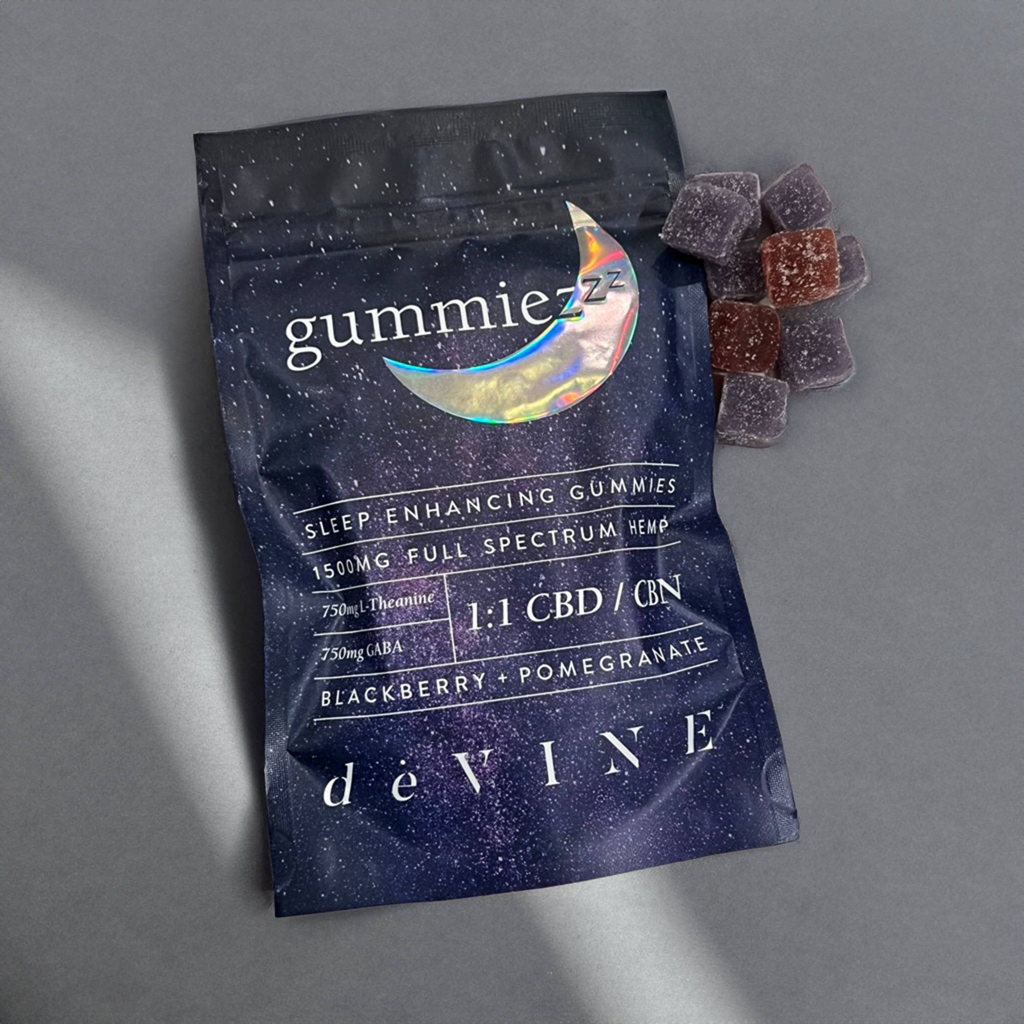 A package of DeVINE Wellness GummieZzz CBD sleep gummies sits on a gray surface with several purple and red gummies nearby. The packaging displays a crescent moon, starry design, and white sleep aid details.